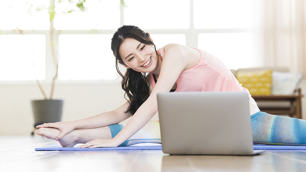 自宅でパソコンを見ながらヨガをしている女性の写真