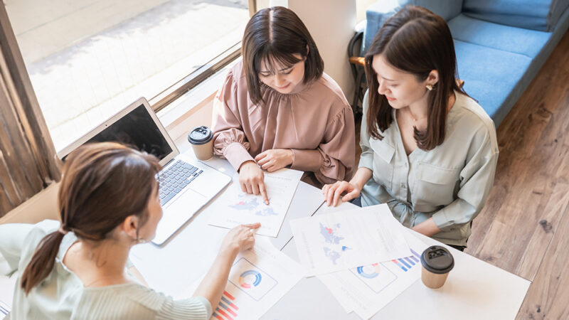 3人の女声が窓際のテーブルで打ち合わせしている様子