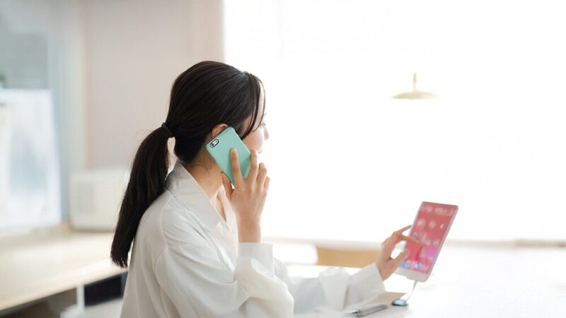 タブレットの画面を見ながら電話している女性の写真