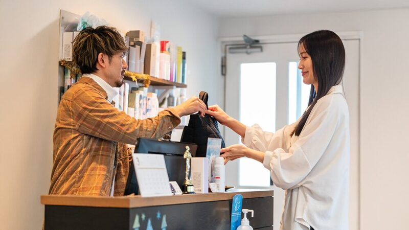 男性スタッフがレジで女性にショッパーを渡している写真
