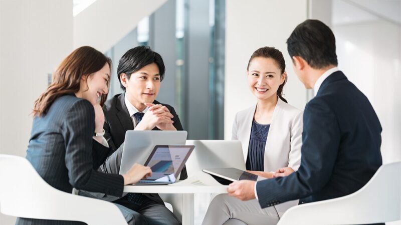 スーツの男女4人がパソコンを前に話し合っている写真