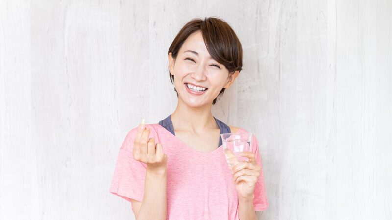 スポーツウェアの女性が笑顔でサプリメントと水をもっている写真