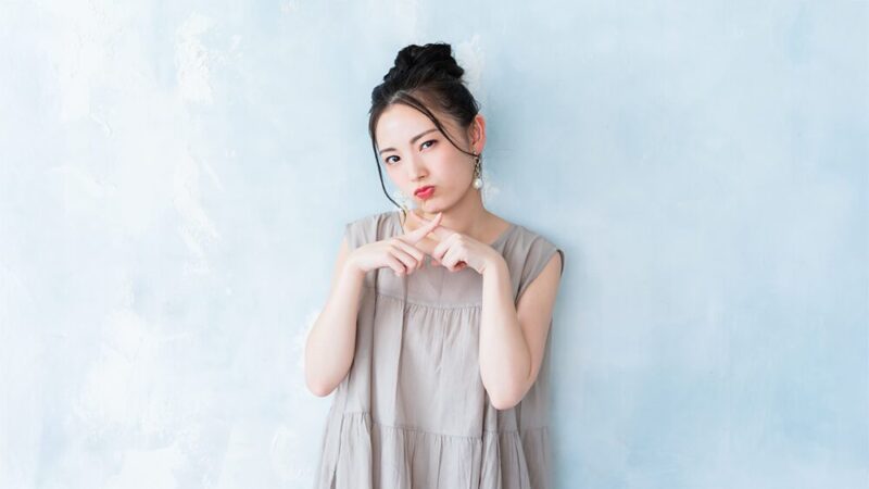 頬を膨らました女性が指でバツを作っている写真
