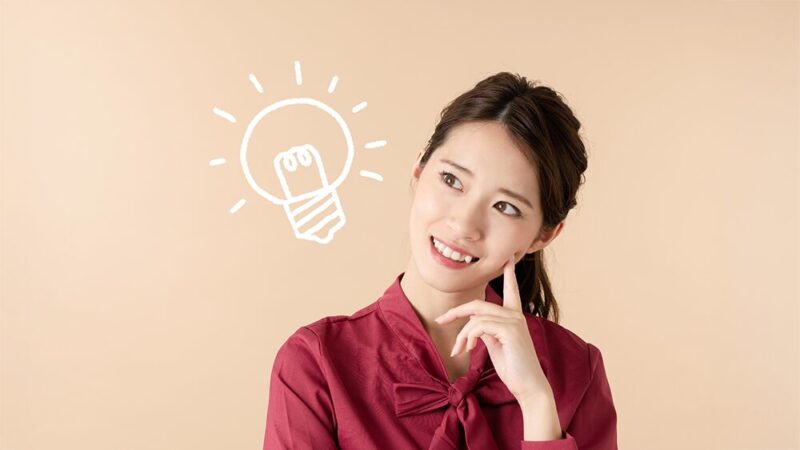 首を傾げ、頬に指をついている女性の横に豆電球のイラストがある写真