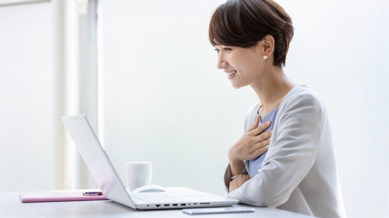 ノートパソコンの前で笑顔の女性が胸に手を当てている写真