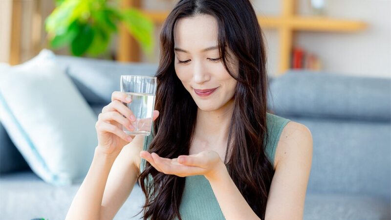 女性がリビングで薬を飲もうとしている写真