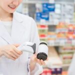 白衣の女性が瓶の商品にバーコードリーダーをかざしている写真