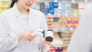 白衣の女性が瓶の商品にバーコードリーダーをかざしている写真