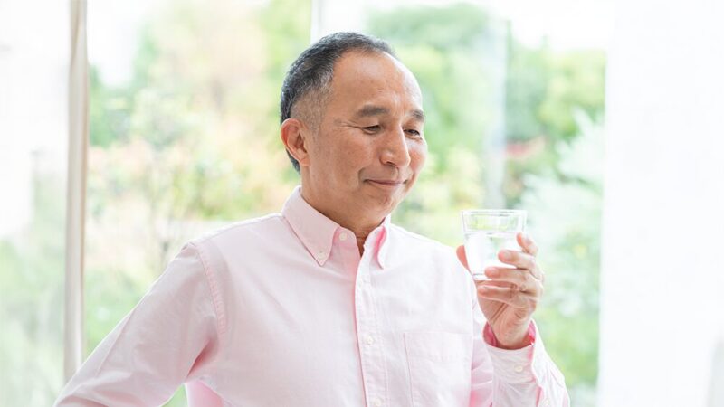 水の入ったコップを持っている高齢男性の写真