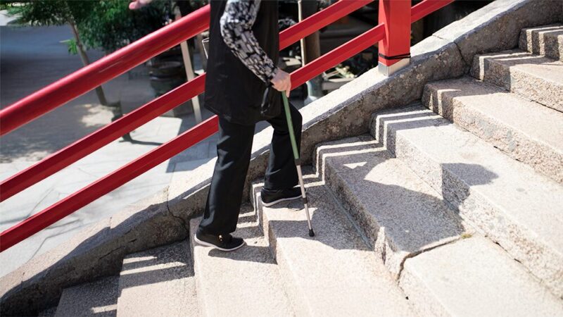杖をついて階段を上がる高齢女性の写真