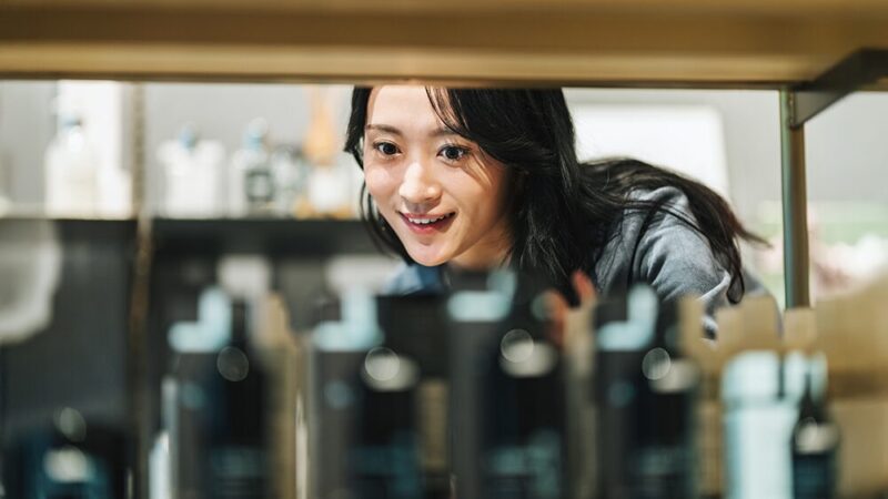女性が笑顔で、棚に並ぶ化粧品を見ている写真