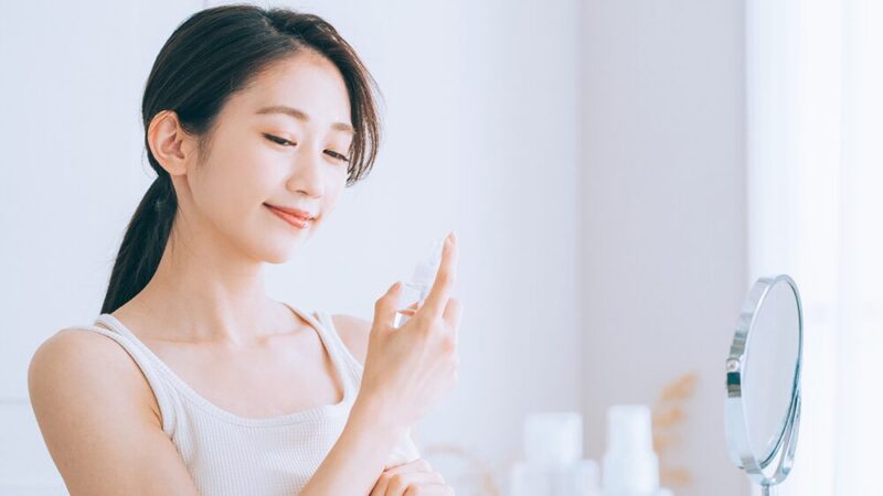 女性が笑顔でミストボトルを手に取り見つめている写真