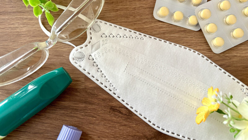 木製の机の上でマスクやメガネ、点鼻薬と錠剤が並んでる写真