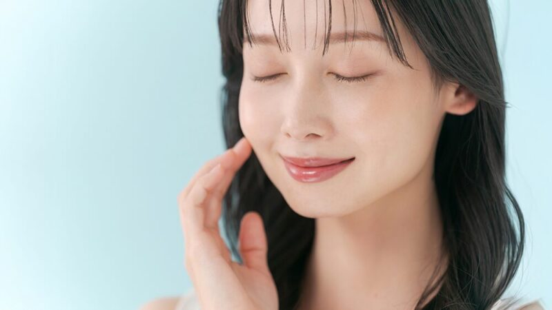 笑顔の女性が頬に手を当てて目を瞑っている写真