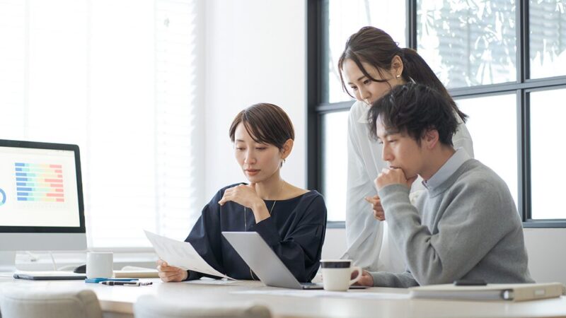 社内で男女3名がパソコンを前に話し合っている写真