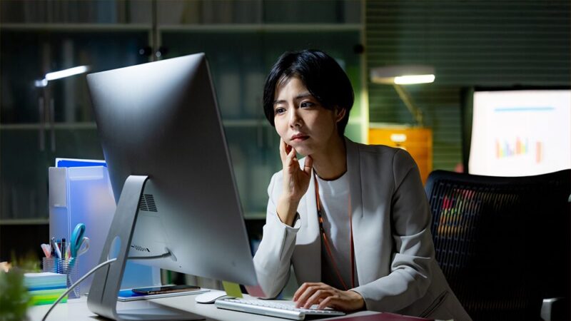 暗いオフィスで頭を抱えている女性の写真