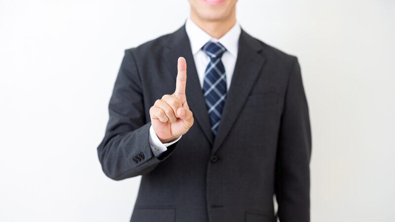 人差し指を上に上げているスーツ姿の男性の写真