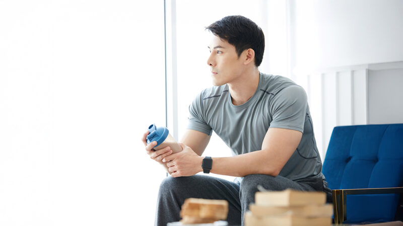 プロテインが入ったシェイカーをもって座っている男性の写真