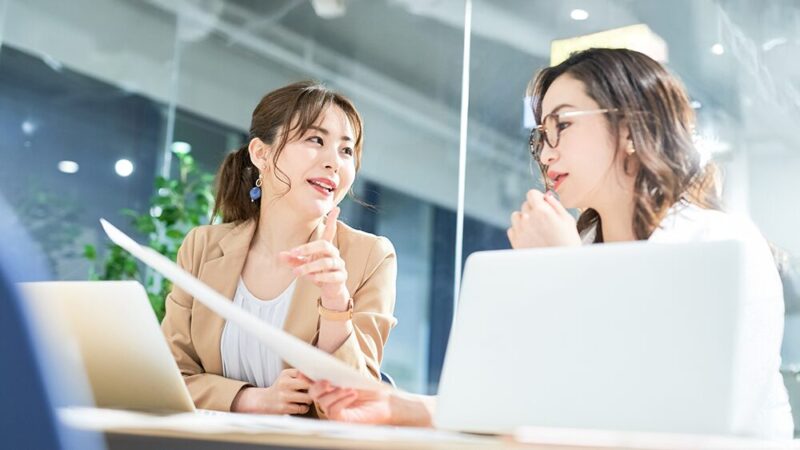 オフィスで女性2人がデータを見て話し合っている写真