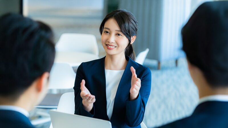 スーツの女性が男性2人に説明している写真