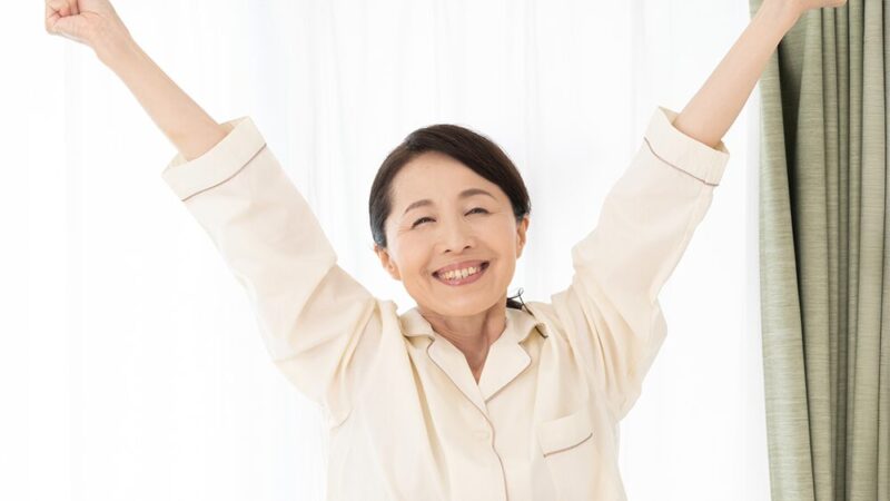 シニア女性がパジャマ姿で笑顔で伸びをしている写真