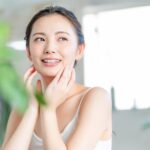植物を背景に、女性が頬に手を添えて笑っている写真