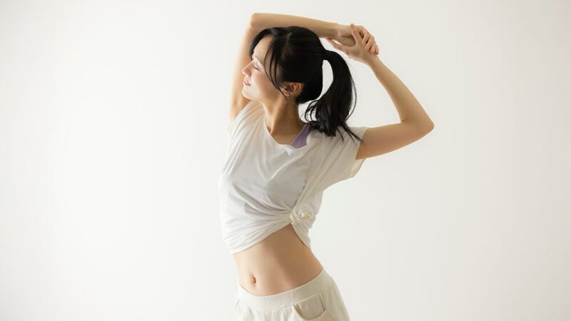 トレーニングウェア姿の女性が伸びをして、くびれが見えている写真