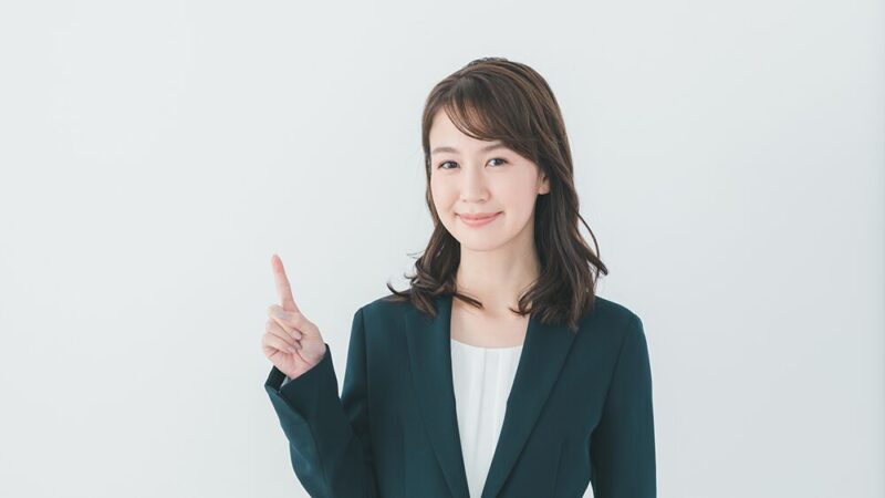 スーツの女性が笑顔で指をさしている写真
