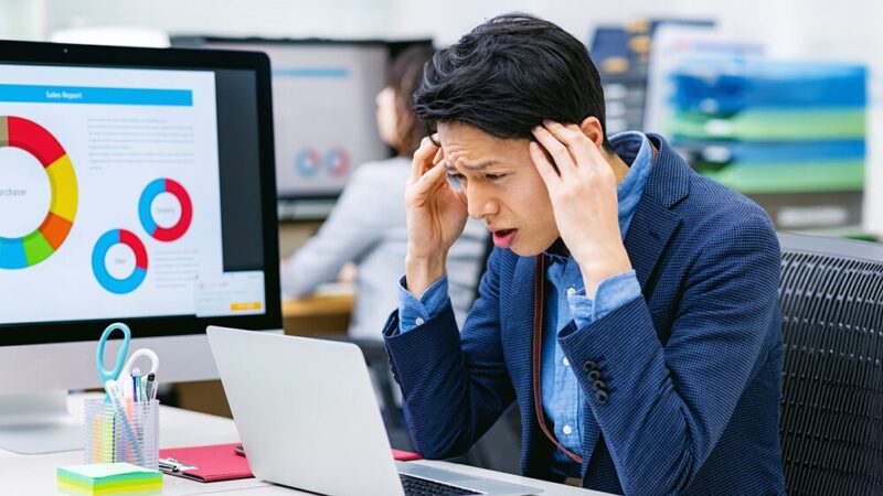 スーツの男性がパソコンの前で頭を抱えている写真