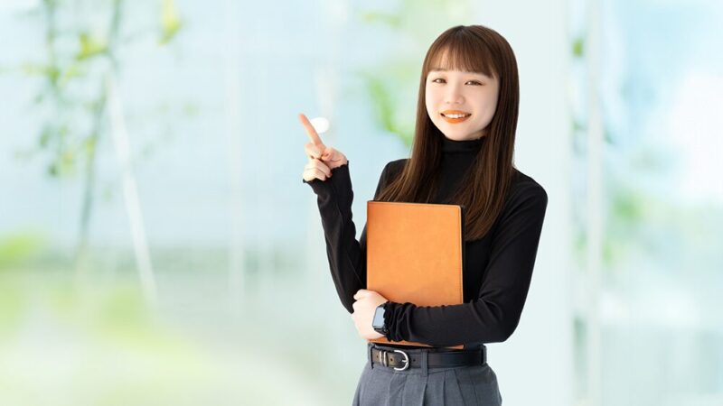 OLが左手に書類を持ち、右手人差し指を指している写真
