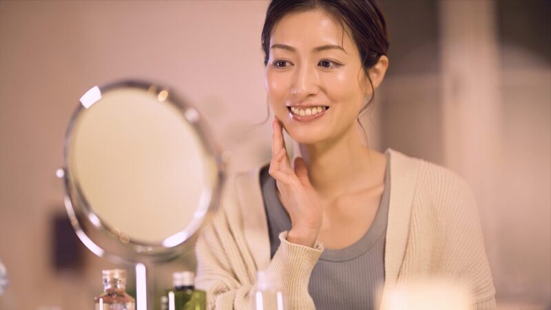 笑顔で鏡で顔を見ている女性の写真
