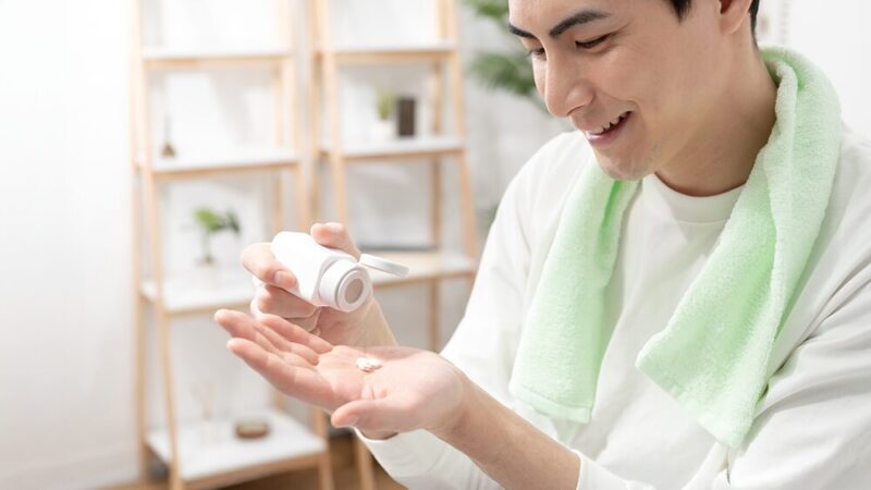 首にタオルをかけた男性が錠剤を手に出している写真