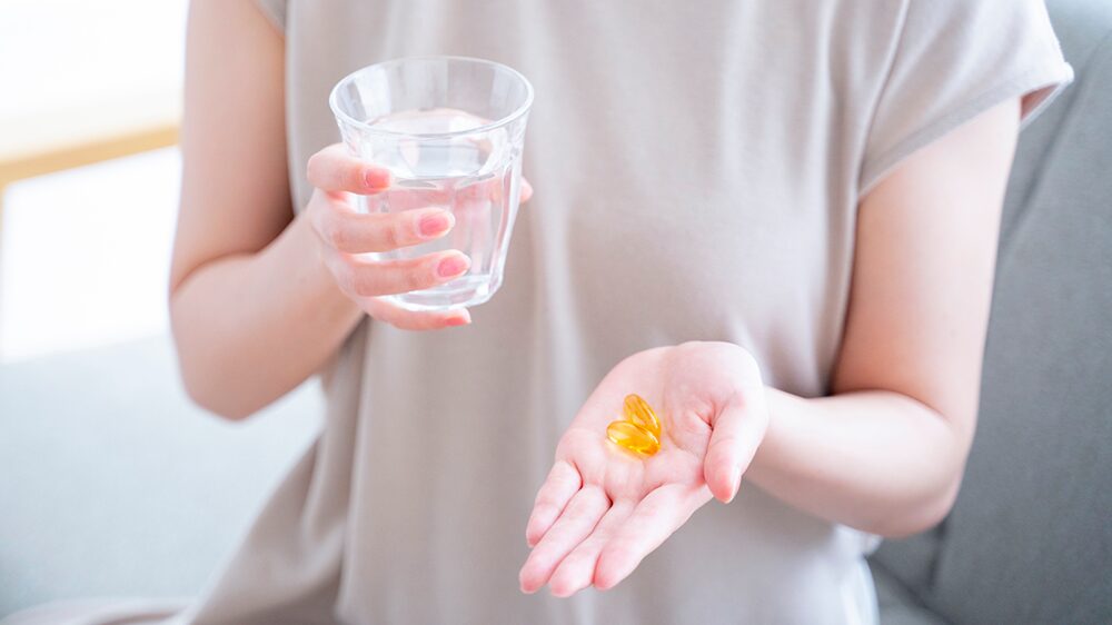 左手にソフトカプセル、右手に水を持っている女性の写真