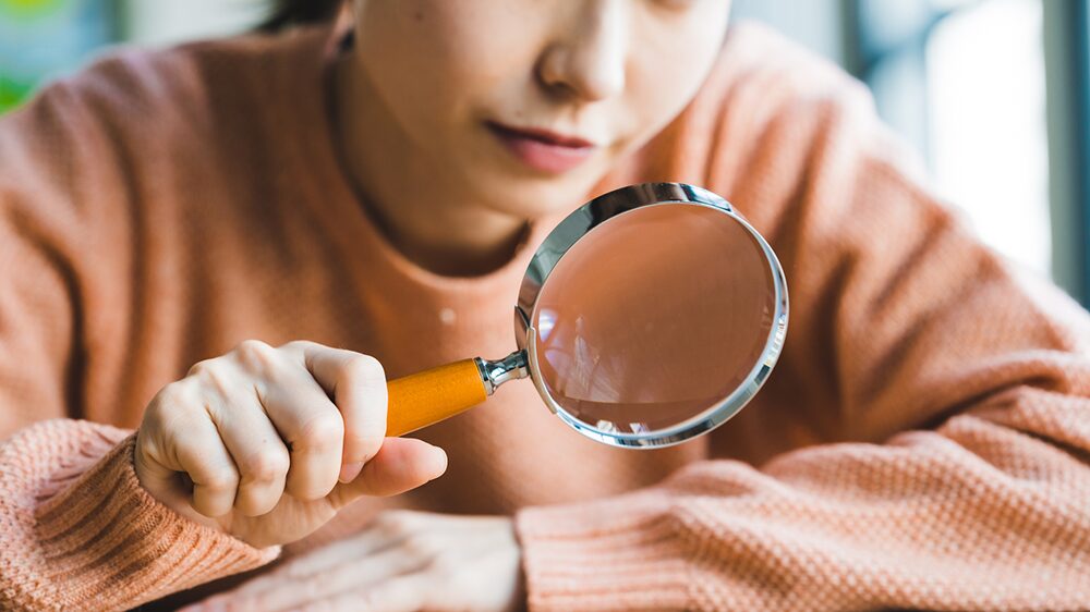 虫眼鏡でじっと見ている女性の写真