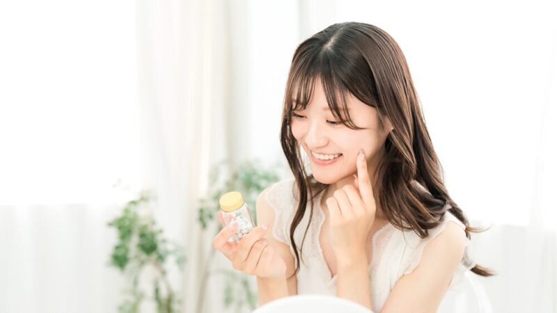 サプリメントを片手に鏡に向かって微笑んでいる女性の写真