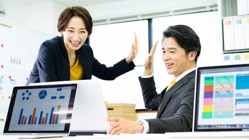 スーツの男女が笑顔でハイタッチしている画像