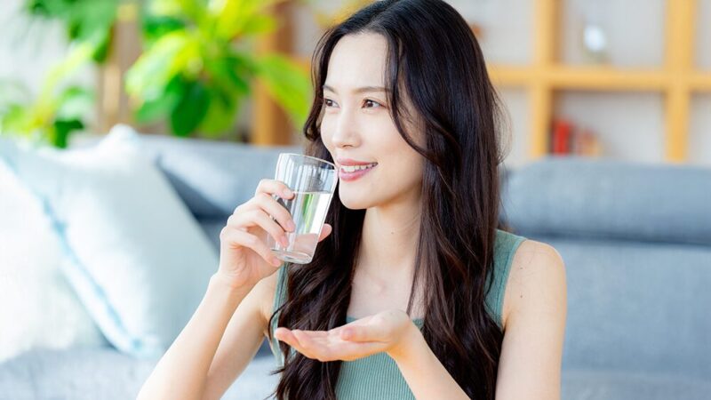 笑顔の女性が水を片手に、サプリメントを飲もうとしている写真