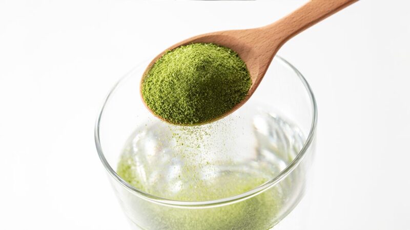 緑の粉末をコップの水に注いでいる写真