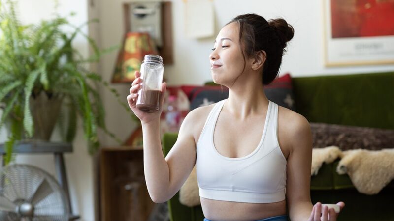 スポーツウェア姿で笑顔でプロテインを飲んでいる女性の写真