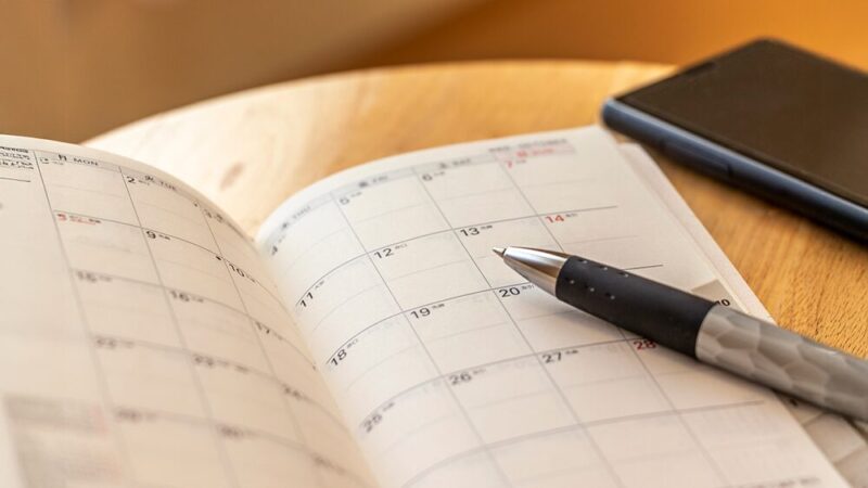 スケジュール帳とペンとスマートフォンの写真