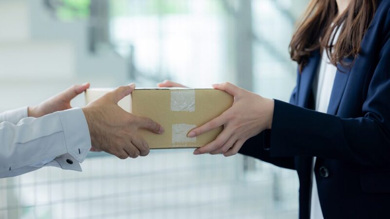 作業着の男性からスーツの女性へと段ボールが渡される写真