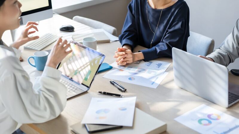 会議室でパソコンと大量のデータを前に話し合っている社員の写真