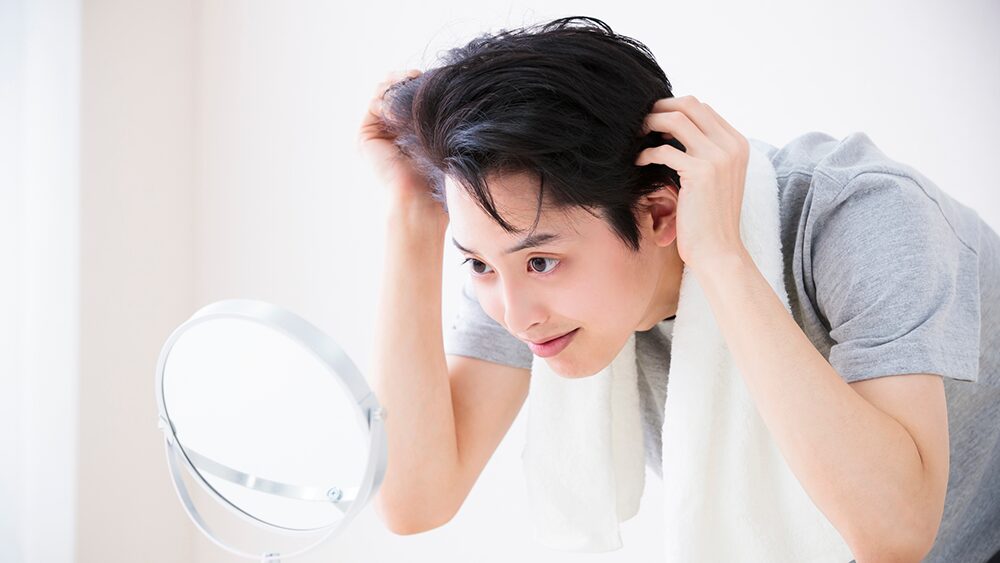 男性が鏡を見て頭髪を気にしている写真