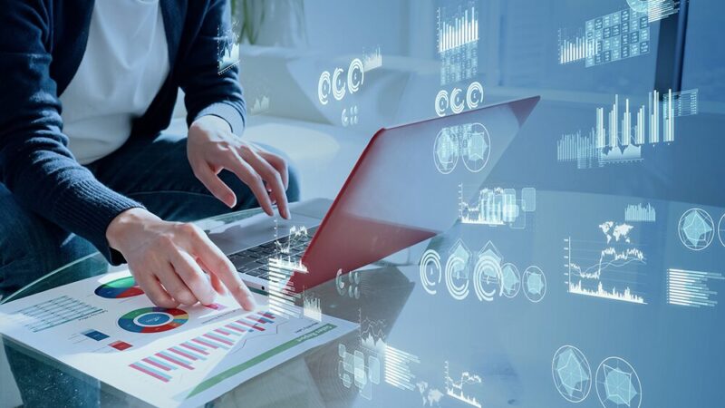 棒グラフや円グラフなどのデータとパソコンを操作する男性の写真