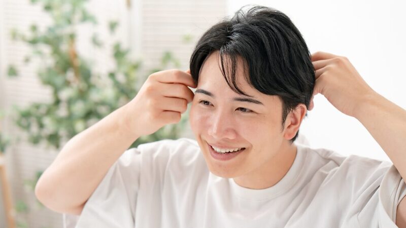 笑顔で髪を触っている男性の写真