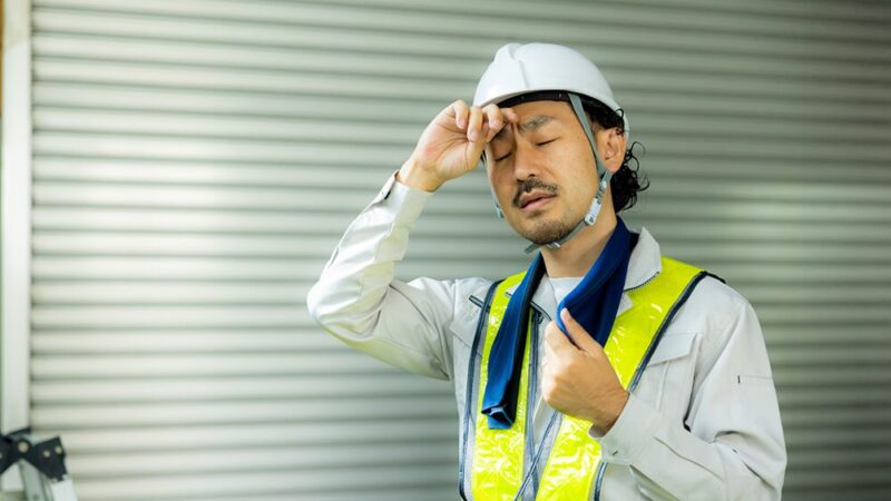 作業着の男性が辛そうに汗を拭っている写真