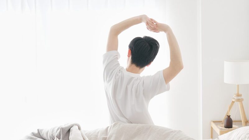 男性が朝日を浴びての伸びをしている写真