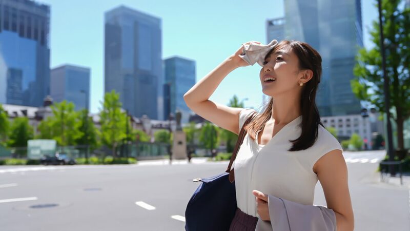 女性会社員が炎天下の下、笑顔で汗を拭っている写真