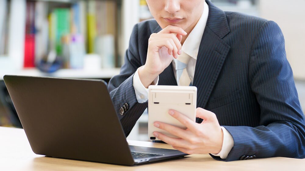 パソコンの前で電卓をもって悩んでいる男性の写真