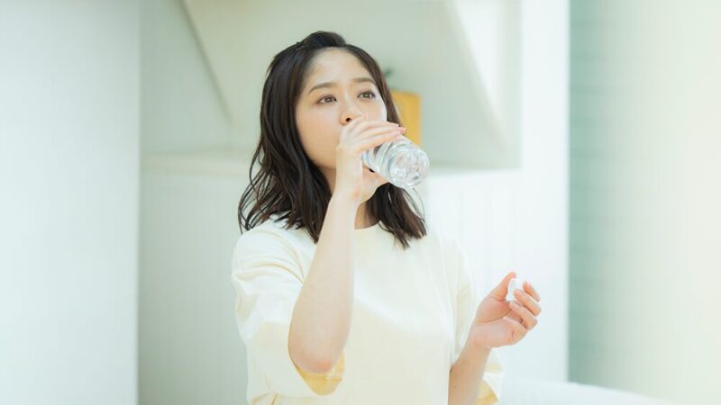部屋着でペットボトルの飲み物を飲んでいる女性の写真